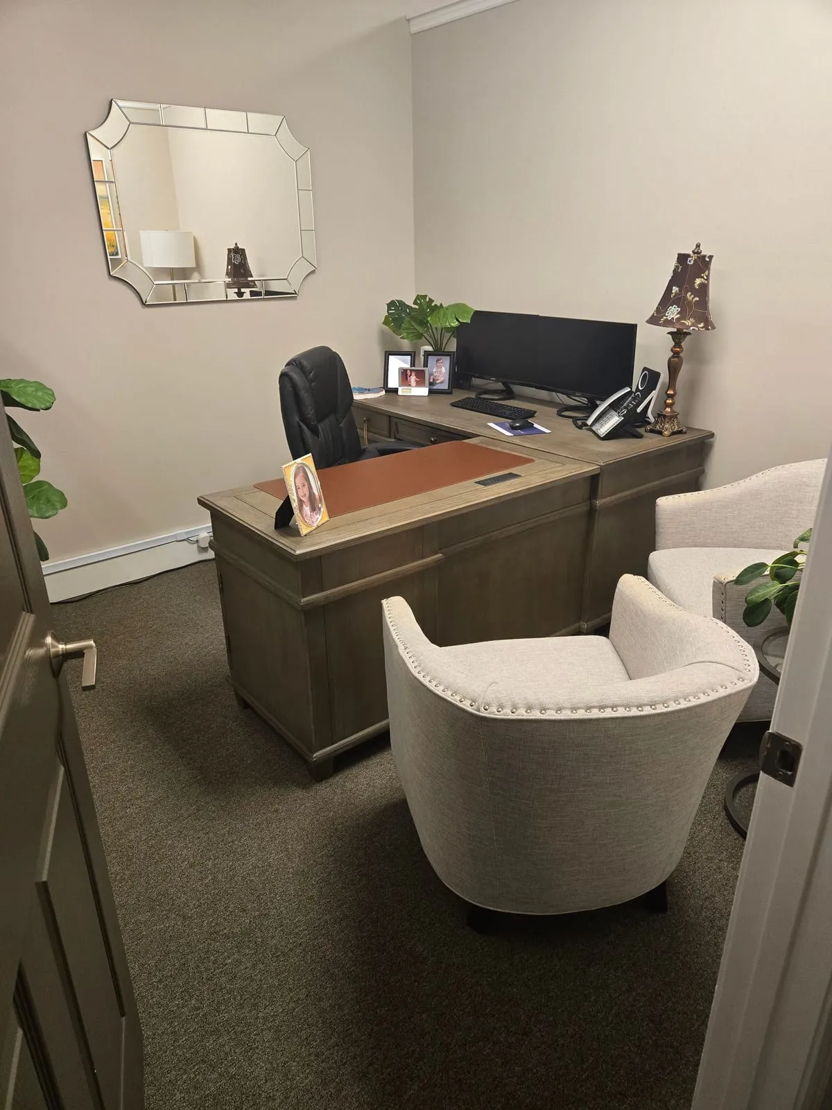 A private office seen from the doorway, with a wood desk and two cream chairs